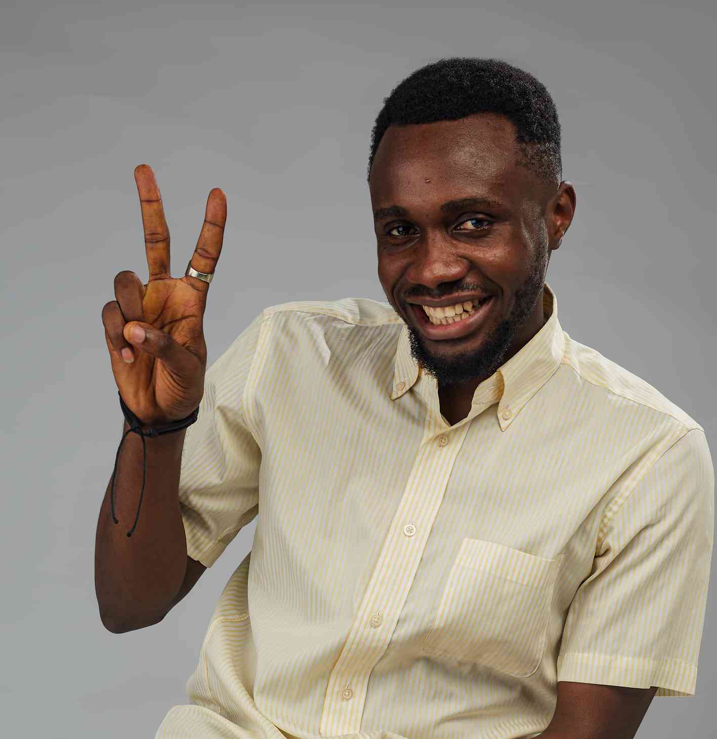  A cheerful man in a striped shirt gives a peace sign while smiling widely at the camera. His expression and gesture radiate positivity and friendliness.