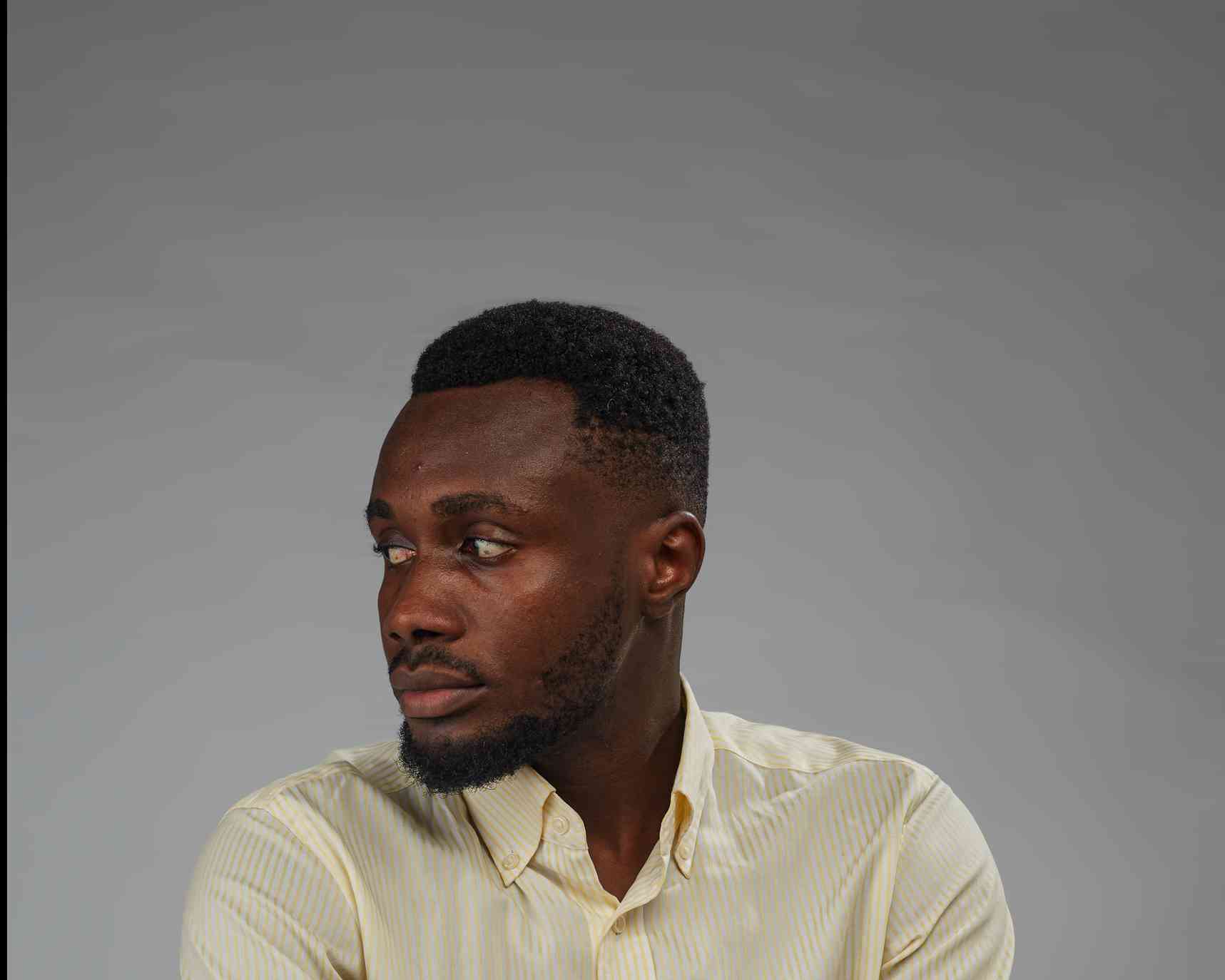 A thoughtful side-profile of a man in a striped shirt, gazing out of frame. The soft lighting and his composed demeanor create a calm, introspective atmosphere.