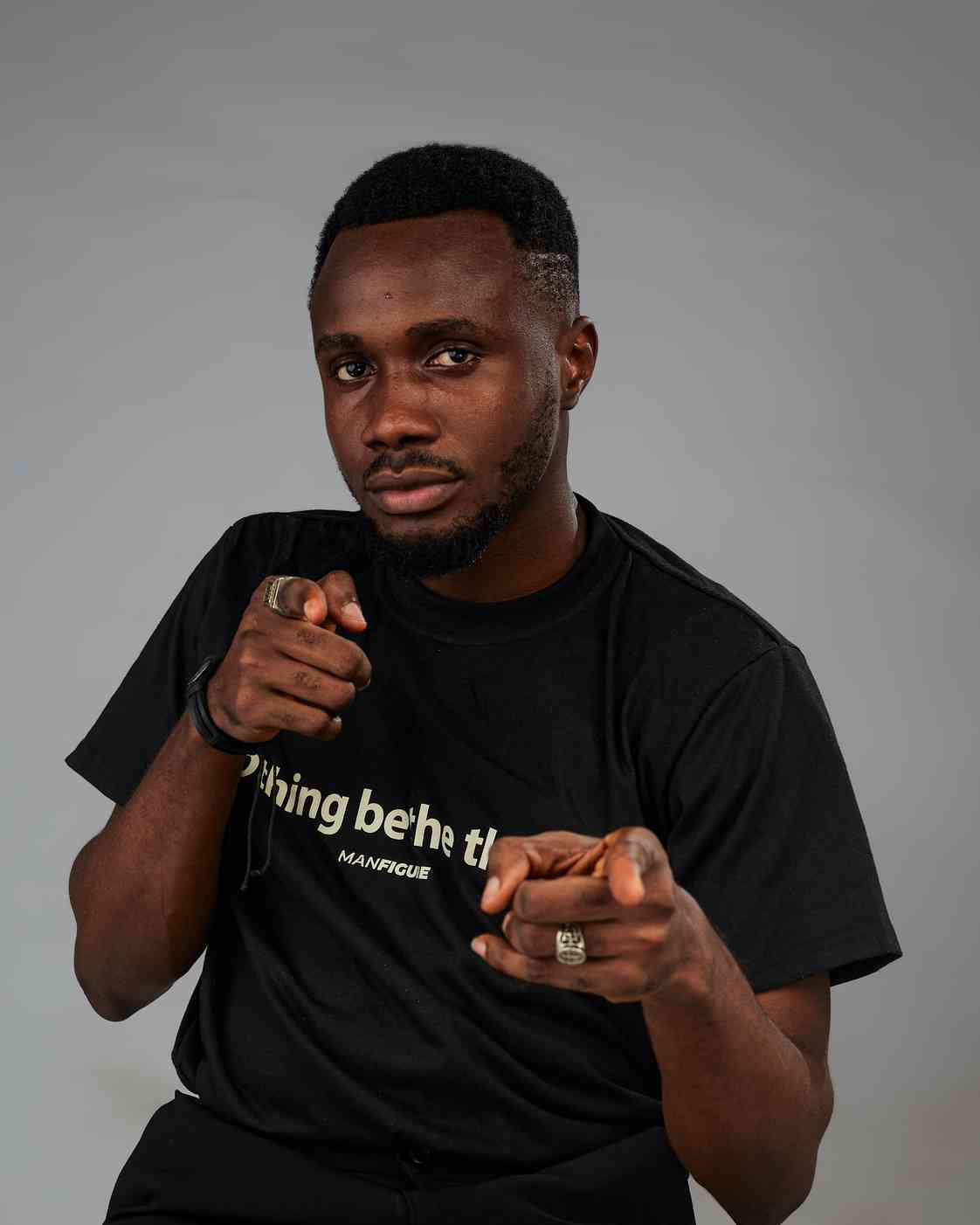 Young man confidently pointing at the camera with both hands, slightly smiling. Wearing a black t-shirt and accessories.