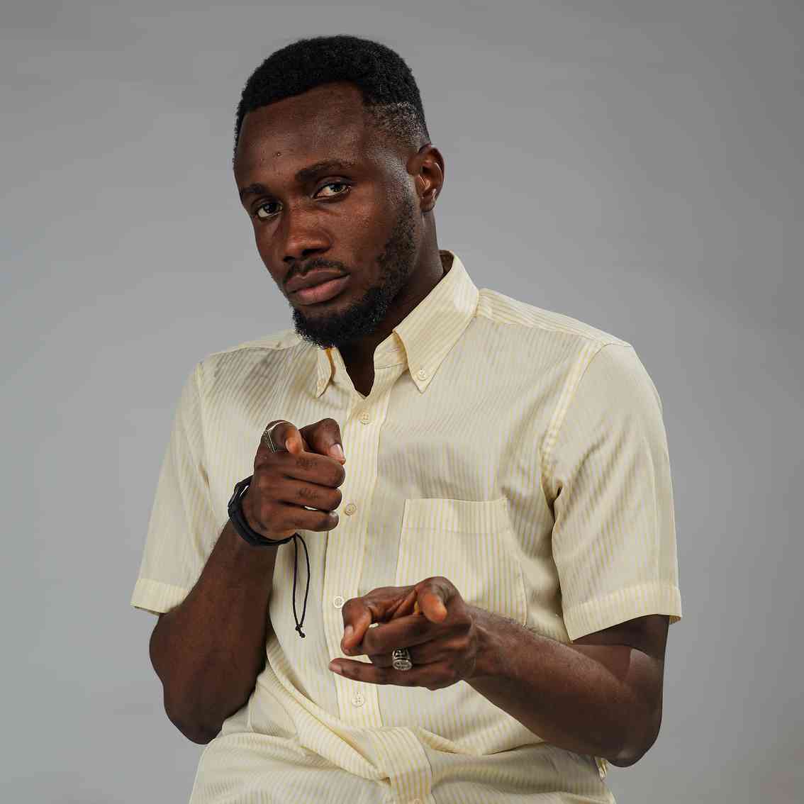 A young man wearing a light yellow shirt poses playfully with finger guns, giving a confident smirk.