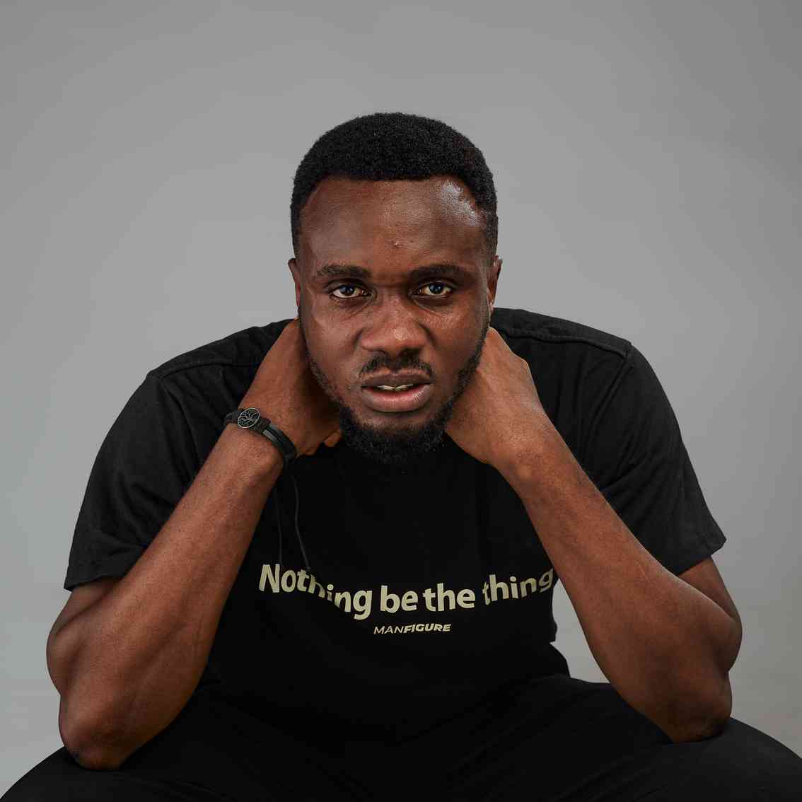 A man in a black t-shirt with the text "Nothing be the thing" grips the back of his neck while glaring intensely at the camera.