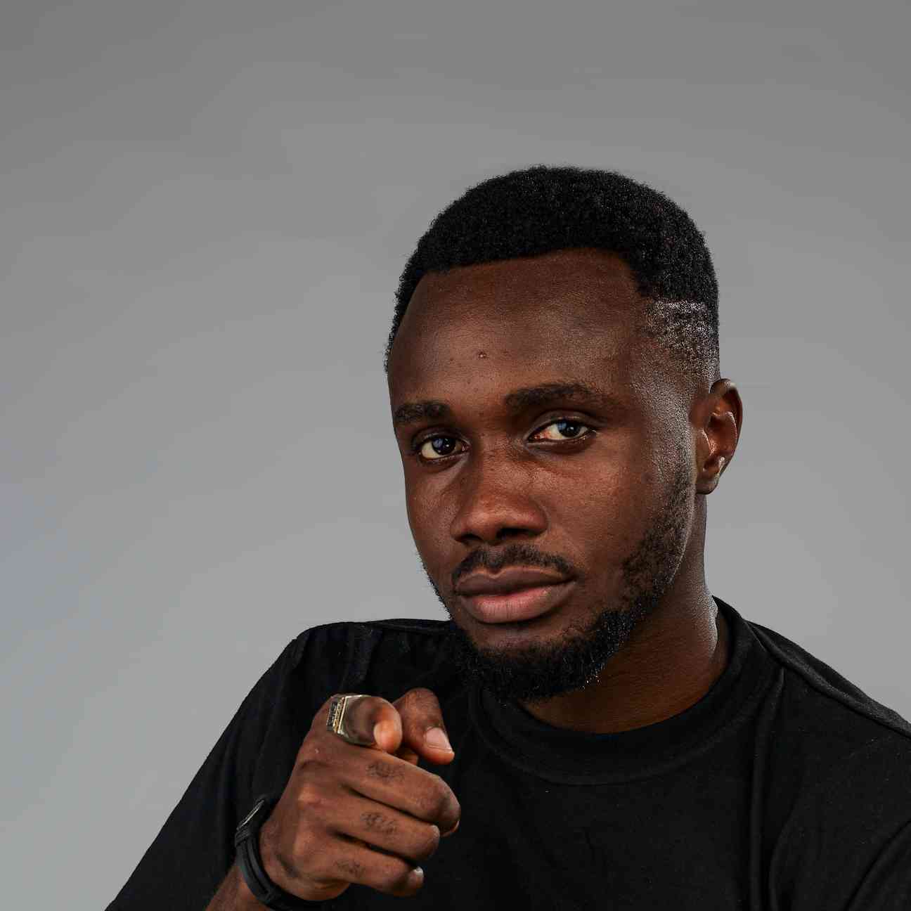 A close-up portrait of a man pointing directly at the camera with confidence, wearing a black tee.